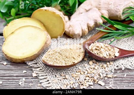 Ground ginger and flakes in two wooden spoons, ginger root on burlap, spicy herbs on a background of an old wooden board Stock Photo