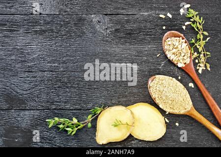 Frame of ground ginger and dry cereal in spoons, two slices of ginger root, thyme sprigs on a black wooden board top Stock Photo