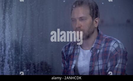 Sad man looking through window during rainy weather, thinking about life problem Stock Photo