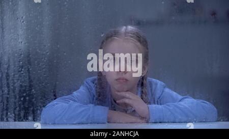 Upset girl looking through rainy hospital window, feeling lonely and insecure Stock Photo