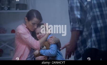 Mother hugging daughter, protecting from angry father, harassment in family Stock Photo