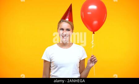 Cheerful lady party horn holding red balloon on bright background, holiday Stock Photo