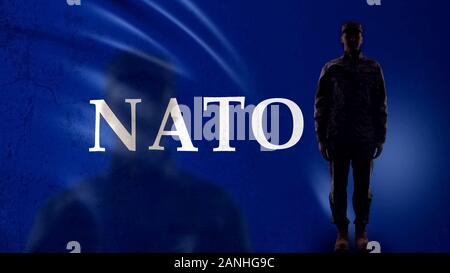 Soldier silhouette standing against NATO flag, military alliance, defense Stock Photo