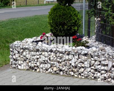 white stone planter in the spring on street corner. galvanized steel mesh fence filled with crashed stone. coniferous deep green Thuja in the center. Stock Photo