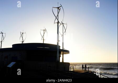 A couple silhouetted against the sea at Cleveleys looking out to sea after the passing of a storm with wind turbines on cafe roof next to them Stock Photo