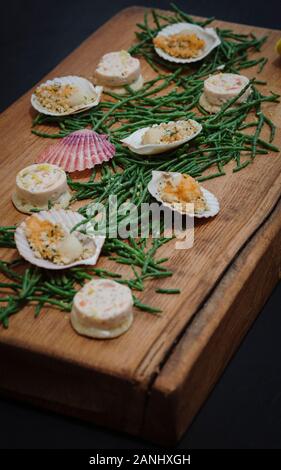 Seafood platter: Canapes served on a wooden board with scallops and samphire and lemon wedges. Top view. Stock Photo