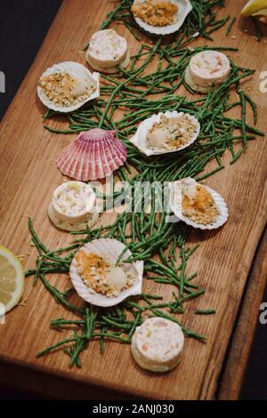 Seafood platter: Canapes served on a wooden board with scallops and samphire and lemon wedges. Top view. Stock Photo