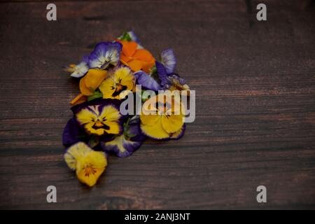 Edible Viola (Violate) flowers on an old dark wooden kitchen worktop Stock Photo