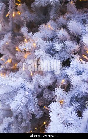 White branches of a fake plastic Christmas tree with lights as a holiday decoration. No eco-friendly decor and harm to nature concept. Stock Photo