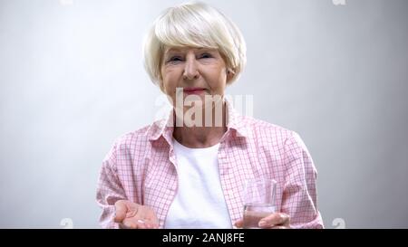 Old lady showing pills and glass of water at camera, pharmacology and healthcare Stock Photo