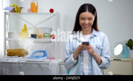 Irresponsible housewife chatting on smartphone, leaving hot iron on board Stock Photo