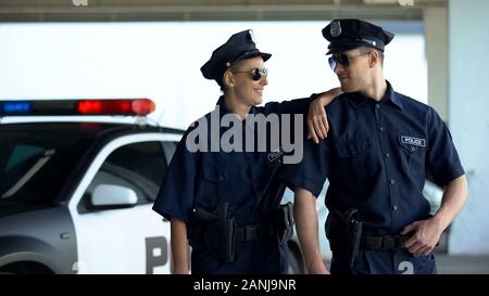 Positive police officers in uniform and glasses smiling together, law and order