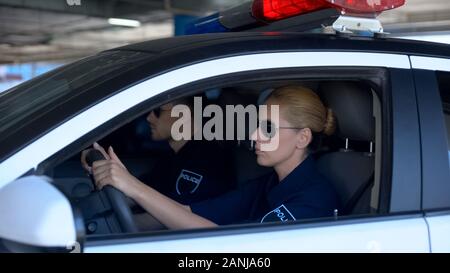 Female and male police officers wearing sunglasses sitting in patrol car, law Stock Photo