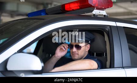 Young policeman adjusting sunglasses sitting in patrol car, responsible job Stock Photo