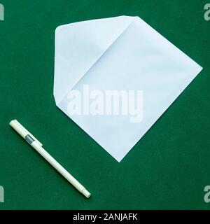 Traditional white letter envelope with ballpoint pen next to it, on a green background Stock Photo