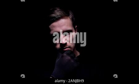 Insane man in gloves touching his chin and smiling, planning bloody murder Stock Photo