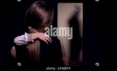 Mum hugging girl, looking at dad entering room, husband tyrant domestic violence Stock Photo