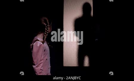 Girl looking at silhouette of criminal entering room, kidnapping concept, horror Stock Photo