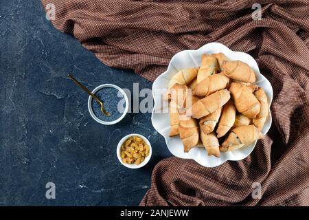freshly baked croissants with poppy seeds and raisins filling on a white plate on a concrete table, flat lay, free space Stock Photo