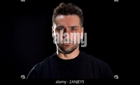 Depressed man looking camera black background, problem disappointment, pain Stock Photo