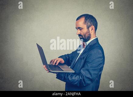 Young handsome mature middle age business man connecting to internet using looking attentively in a laptop. Mixed race bearded guy isolated on gray st Stock Photo