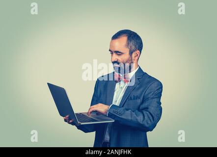 Young handsome mature middle age business man connecting to internet using looking attentively in a laptop. Mixed race bearded guy isolated on green s Stock Photo