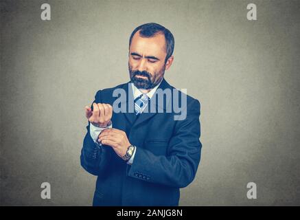 Half body portrait of handsome bearded man in formal wear fastens cufflinks, the buttons of his shirt sleeve standing isolated on gray wall background Stock Photo