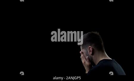 Depressed man covering face by hands on dark background, mistake regret, problem Stock Photo