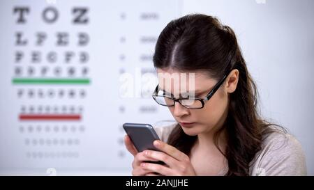 Pretty woman in eyeglasses holding smartphone, technology influence on vision Stock Photo