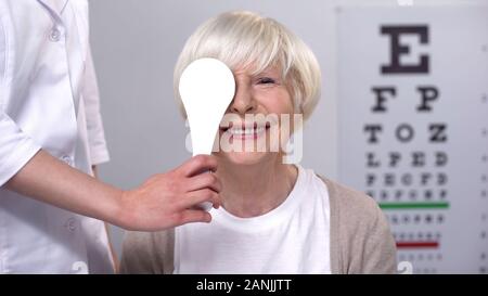 Optician closing elderly ladies eye, maintaining satisfactory eyesight, test Stock Photo