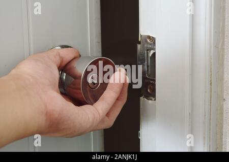 hand twisting silver knob to opened door in dark room Stock Photo