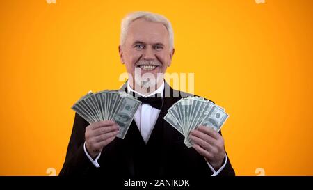 Wealthy elderly man in suit holding dollars and smiling, successful business Stock Photo