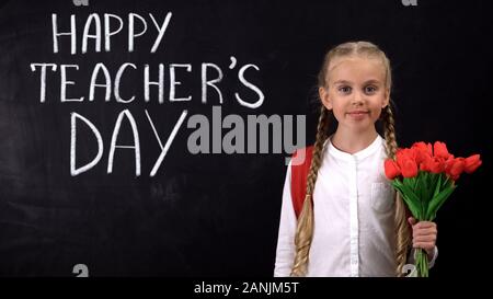Smiling girl with tulips bouquet standing against blackboard, happy teachers day Stock Photo