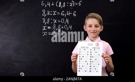 Diligent smiling schoolboy showing excellent test, math exercise written behind Stock Photo