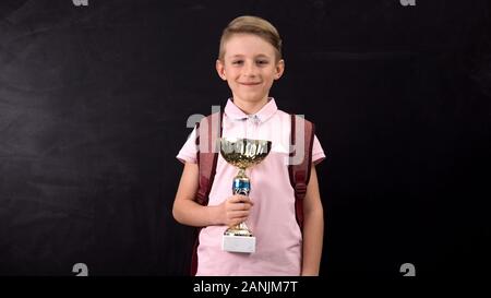 Smiling primary schoolboy holding cup award, championship winner, success Stock Photo