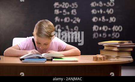 Smart schoolboy solving task, math exercises written on blackboard behind Stock Photo