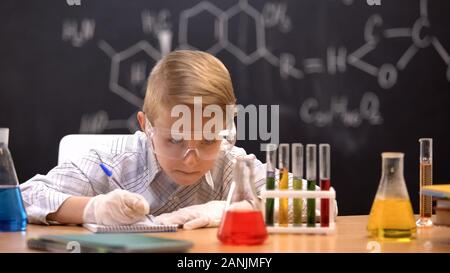 Schoolboy looking at sediment in flask and writing results, chemistry lesson Stock Photo