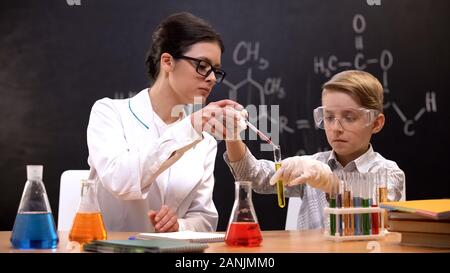 Teacher helping schoolboy dripping red substance in test tube, chemistry lesson Stock Photo