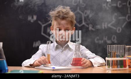 Shocked schoolboy sitting in cloud of smoke, explosion during experiment Stock Photo