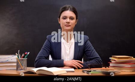 Tired female teacher looking to camera sitting in class, favorite occupation Stock Photo