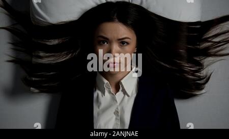 Serious woman in suit lying in bed, overworking concept, stressful lifestyle Stock Photo