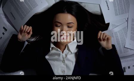 Businesswoman lying in bed among documents, successful contract, happy to finish Stock Photo