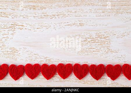 Row of red felt valentine hearts on a white wood textured surface. Valentine greeting card with copy space. Romance and love concept. Top view. Stock Photo