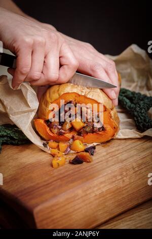 Stuffed Roasted Butternut squash with a kale & chickpea salad. Healthy vegan food served on an orange tray with black background. Top view / flat lay Stock Photo