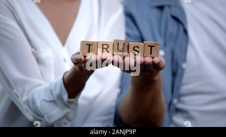 Couple in love holding trust word on wooden cubes on palms, family relations Stock Photo