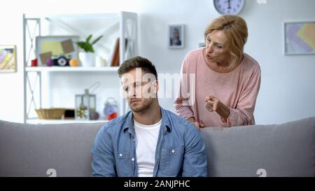 Nervous mother talking to adult son sitting on sofa at home, family conflict Stock Photo