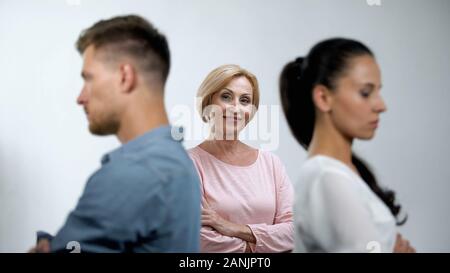 Satisfied mother looking at couple in quarrel standing back to each other Stock Photo