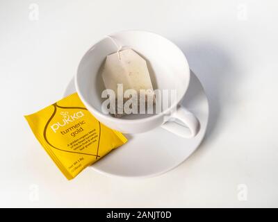 Herbal tea bag inside white cup on saucer. Stock Photo