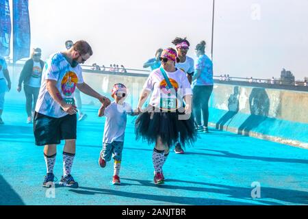 April 6 2019 Tulsa USA Family of mother father and little boy in matching costumes all holding hands and laughing in color - holi run blue powder s Stock Photo