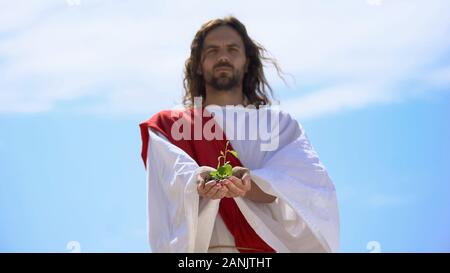 Man in robe showing sprout against sky, nature saving, environmental problems Stock Photo